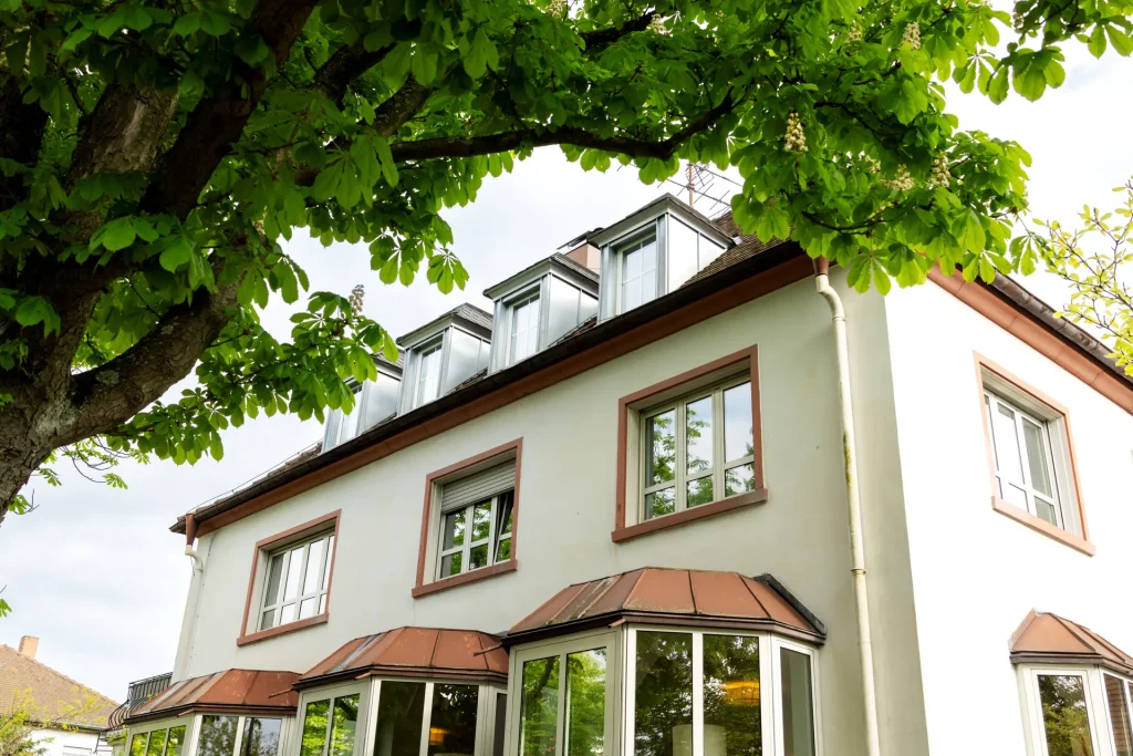 Helles Wohnhaus mit Erkerfenstern und Dachgauben unter Bäumen, Immobilienbewertung in Georgsmarienhütte