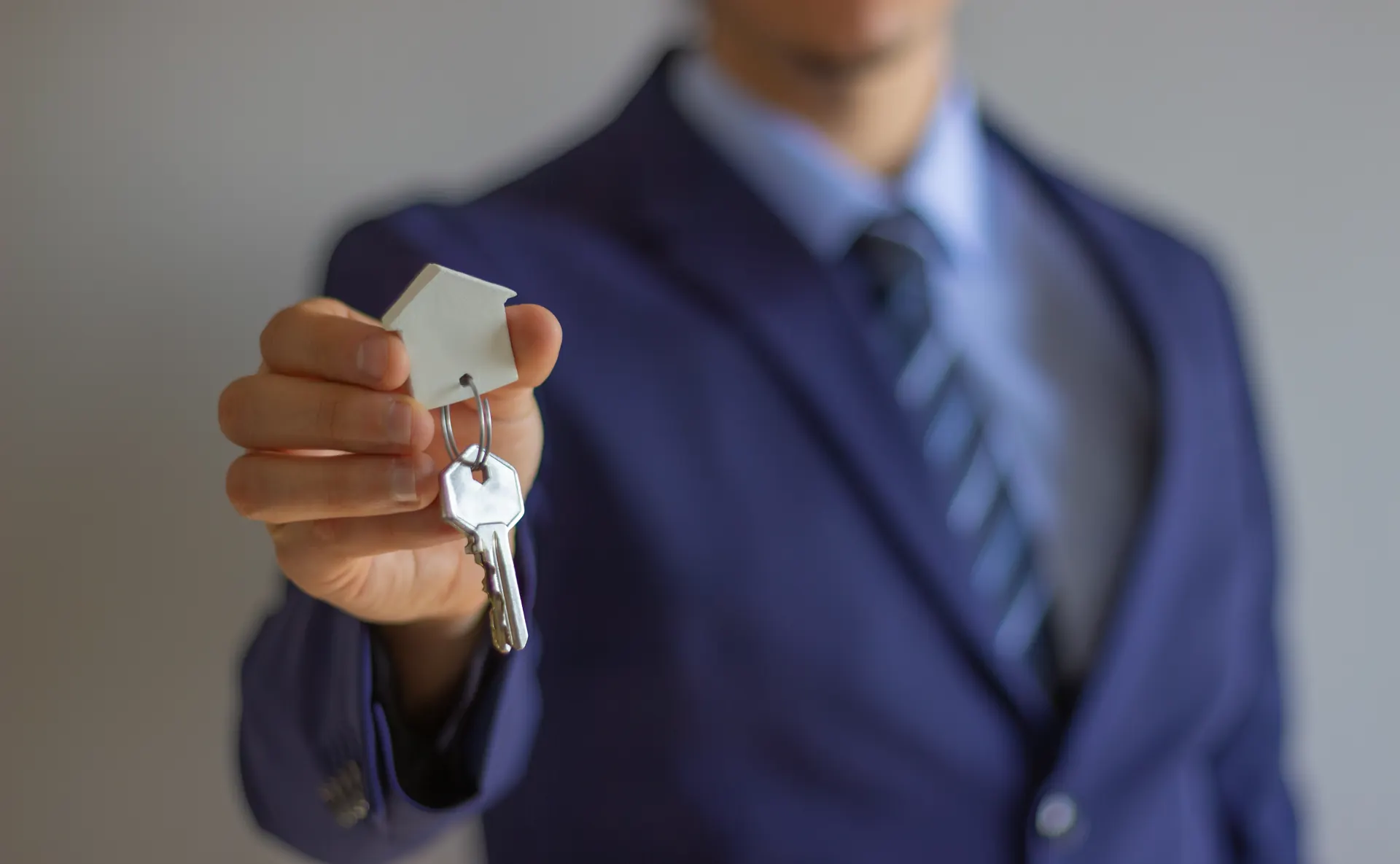 Makler im Anzug überreicht Hausschlüssel bei der Schlüsselübergabe nach dem Immobilienverkauf am Westerberg in Osnabrück
